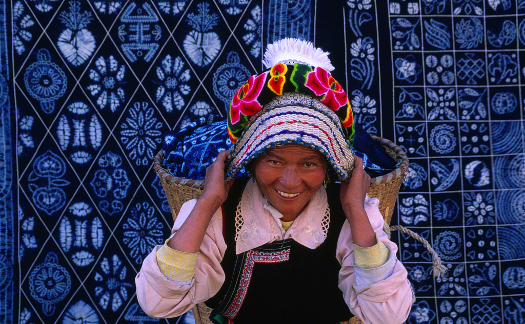 一位白族妇女背着篮子，站在蜡染布前。图/视觉中国